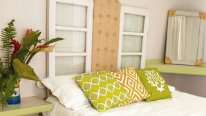 Ein Bett mit gemusterten Kissen, eine Pflanze, ein Fenster mit dekorativem Rahmen und ein gefliestes Zimmer.