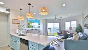 A modern kitchen with a central island, a dining area with a table and chairs, a living room with a sofa, and a balcony with a view. - Keys Escape | Oceanfront Resort Condo | Sleeps 6 (Tavernier)