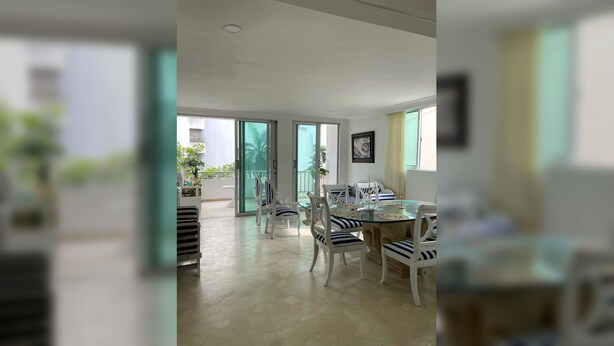 A spacious dining area with a glass table and white chairs, a balcony with plants, and a view of the outside. - Prime Bocagrande 3BR with AC, Parking, Near Beach & Bay Tours (Cartagena de Indias)