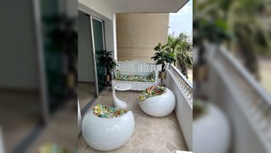 A balcony with a white bench, two white planters with tropical plants, and a glass door leading to an interior space. - Prime Bocagrande 3BR with AC, Parking, Near Beach & Bay Tours (Cartagena de Indias)