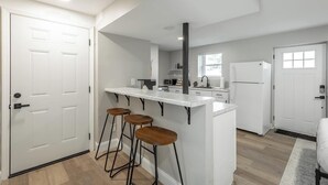 Een moderne keuken met witte kasten, een centraal kookeiland met krukken, een ingebouwde oven en een koelkast.