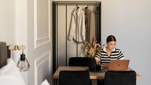 Una habitación con una mesa de comedor, sillas, una computadora portátil, un jarrón con plantas secas y un perchero con colgadores.