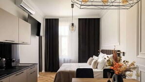 Una habitación de hotel moderna con kitchenette, una cama con cabecera, una mesa de comedor y un jarrón decorativo.