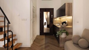 A modern apartment with a wooden staircase, a kitchen with a built-in oven, a sofa, and a potted plant. - L23 Boutique 18B | City Center (Kraków)