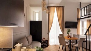 A modern living room with a sofa, dining table, chairs, a coffee table, a TV, and a staircase. - L23 Boutique 18B | City Center (Kraków)