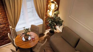 En hyggelig opholdsstue med et rundt træbord, beige sofa og en potteplante.