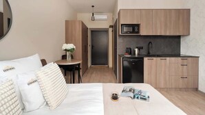 Hotelkamer met een bed, een klein tafeltje met een bloemetje in een vaas, een kitchenette met een magnetron en een koffiezetapparaat.