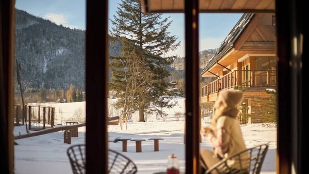 En vy från ett fönster med träinredning, som blickar ut över ett snötäckt landskap med träd och en byggnad.