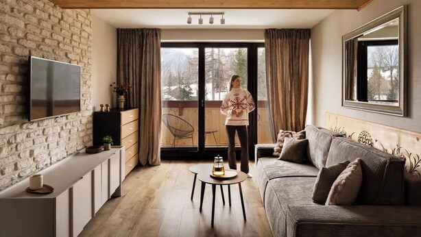 A living room with a TV, sofa, and a person standing by a sliding glass door. - Butorowy Residence | Sauna & Gym | Mountain View (Kościelisko)