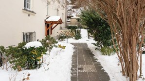 Un sentier enneigé mène à un bâtiment agrémenté d’une pergola en bois et d’un petit jardin.