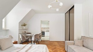 Une pièce moderne et bien éclairée, comprenant un lit, un canapé, un coin repas et une cuisine visible à travers une porte ouverte.