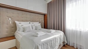 Una habitación de hotel moderna con una cama grande, un cabecero de madera y vistas a la ciudad a través de cortinas translúcidas.