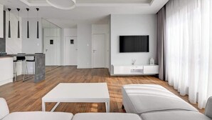 Una sala de estar moderna con un sofá blanco, una mesa de centro, un televisor y una zona de comedor con barra.