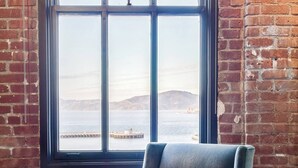 A room with a large window, a blue armchair, a small table, and a brick wall. - Wonderful 2-bedroom apartment with AC in San Francisco (San Francisco)
