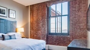 A hotel room with a brick wall, a large window, a bed with white linens, and a blue headboard. - Wonderful 2-bedroom apartment with AC in San Francisco (San Francisco)