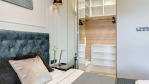 A modern hotel room with a tufted headboard, a bedside table with a lamp, a bed with pillows, a glass shower enclosure, and a built-in wardrobe. - Brabank Superior | Riverside & Balcony | Parking (Gdańsk)