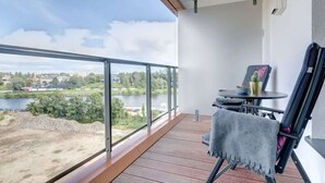 A balcony with a view of a river and cityscape, a table with chairs, and a small potted plant. - Brabank Superior | Riverside & Balcony | Parking (Gdańsk)