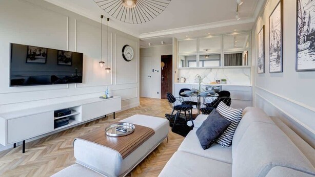A modern living room with a flat-screen TV, a dining area, and a kitchen in the background. - Brabank Superior | Riverside & Balcony | Parking (Gdańsk)