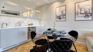 A modern kitchen with white cabinetry, a dining area with a round table and black wire chairs, and two framed black and white maritime paintings on the wall. - Brabank Superior | Riverside & Balcony | Parking (Gdańsk)