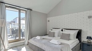 Quarto moderno com uma cama grande, vista por uma porta deslizante e uma parede de tijolos brancos.