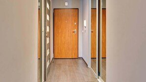 Un couloir avec une porte en bois, une cloison vitrée et un interrupteur sur le mur.