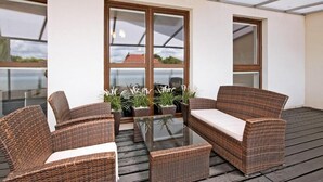 Un espace extérieur aménagé, abrité et doté de mobilier en osier et de tables en verre, de grandes fenêtres et de plantes en pot.