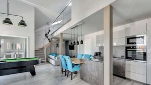 Eine moderne Küche mit integrierten Geräten, ein Essbereich mit blauen Stühlen und ein Billardtisch.