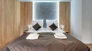 Ein modernes Hotelzimmer mit einem großen Bett, Wandverkleidung aus Holz und einer zentralen Lichtinstallation.