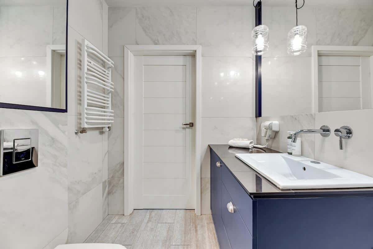 A modern bathroom with a white sink, a mirror, a towel rack, and a door.