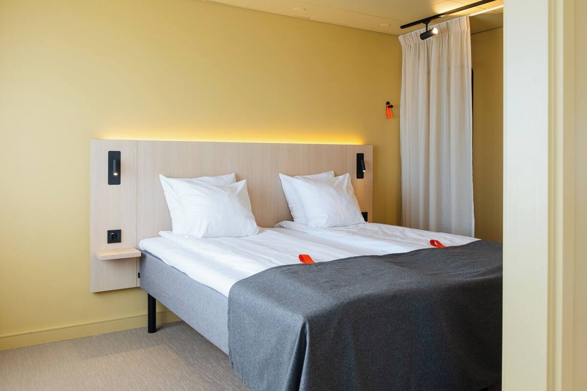 Quarto de hotel com cama, mesas de cabeceira, cabeceira e cortina.