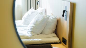 Un lit bien fait, avec du linge de lit blanc et des oreillers, une tête de lit en bois et une table de chevet sur laquelle repose un livre.