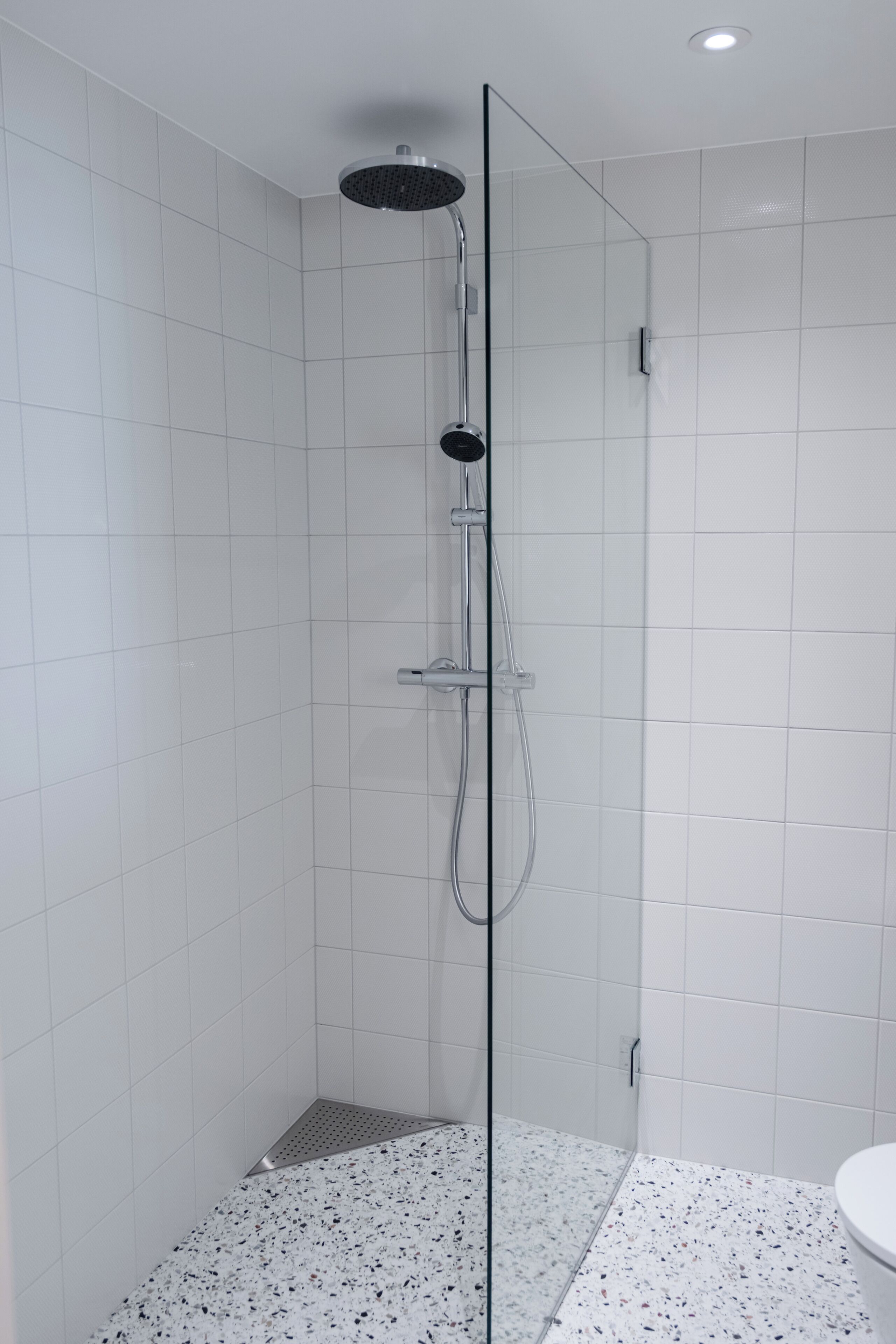 Une douche avec une paroi en verre, des murs recouverts de carreaux blancs et un sol à motifs.
