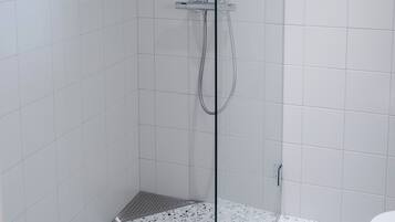 Une douche avec une paroi en verre, des murs recouverts de carreaux blancs et un sol à motifs.