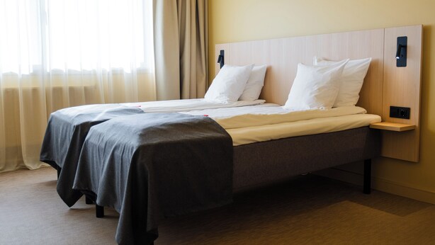 A hotel room with a double bed, a bedside table, a nightstand, and a window with curtains.