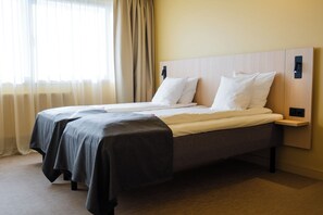 Quarto de hotel com cama de casal, mesa de cabeceira e janela com cortinas.