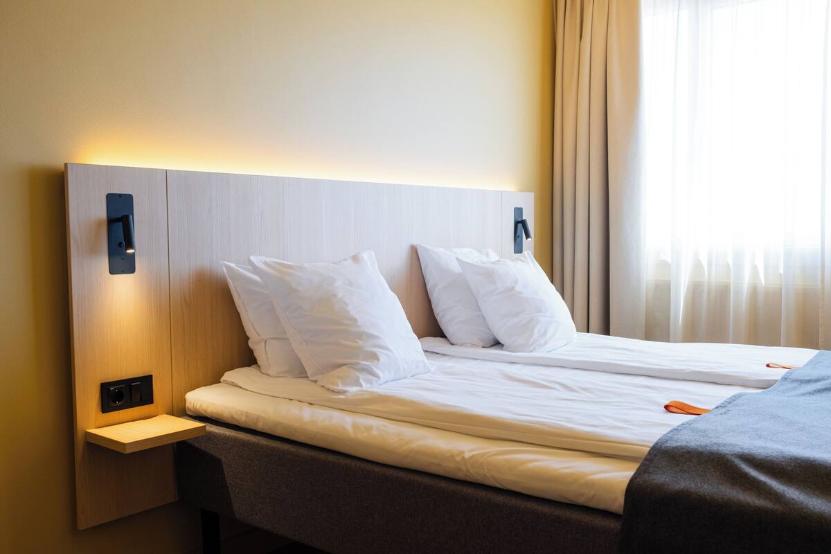 Quarto de hotel com cama, mesas de cabeceira e cortinas.