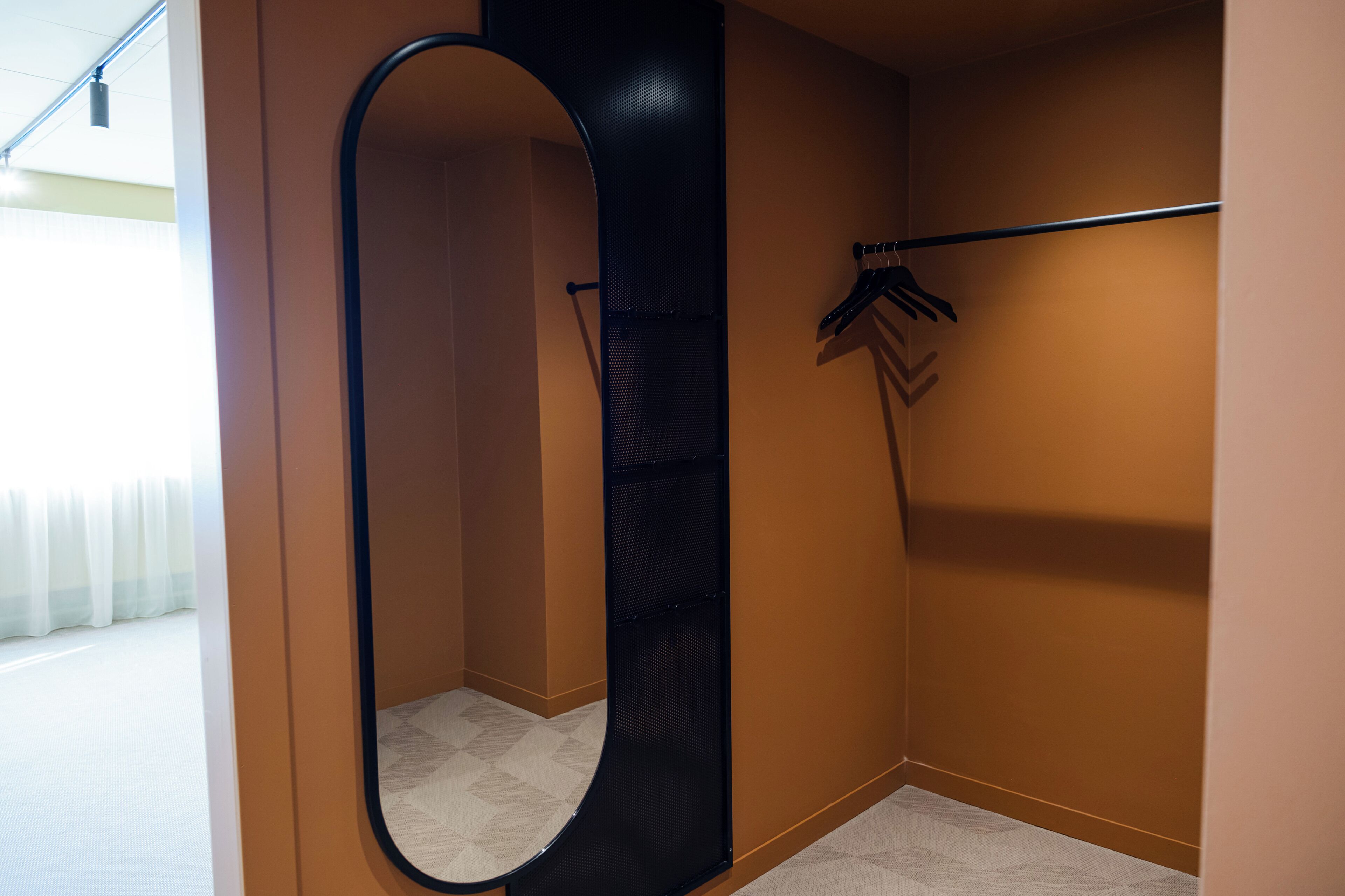 Un coin de pièce avec un miroir incurvé, un portant à vêtements et un sol à motifs.