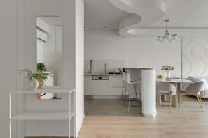 Eine moderne Küche mit weißen Schränken, einer Essecke mit rundem Tisch und Stühlen sowie einem großen Spiegel an der Wand.