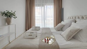 Habitación de hotel con cama, mesita de noche, planta en maceta, ventana con cortinas y bandeja con frutas y una bebida.