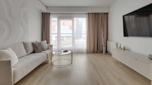 Una sala de estar moderna con un sofá, una mesa de centro redonda, un televisor y vistas amplias a través de grandes ventanales.