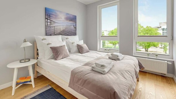 A bedroom with a bed, a nightstand, a painting, and large windows. - Navio with Balcony | Seaside (Gdańsk)