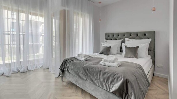 A bedroom with a large bed, sheer curtains, and a modern light fixture. - Nadmotławie C14 | Riverside | Sauna & Gym (Gdańsk)