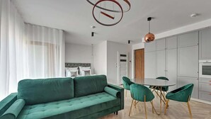 A modern living room with a green sofa, a round dining table with green chairs, and a kitchen area with grey cabinets. - Nadmotławie C14 | Riverside | Sauna & Gym (Gdańsk)