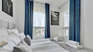 Habitación de hotel con cama, almohadas, ventana con cortinas e imagen enmarcada en la pared.