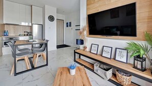 Una sala de estar moderna con televisor, zona de estar y cocina al fondo.
