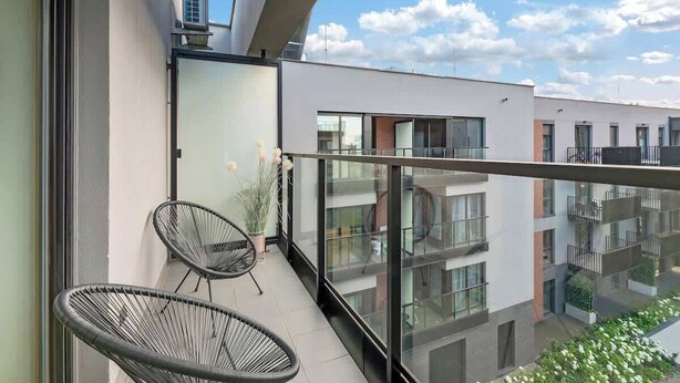 A balcony with two black wire chairs, a potted plant, and a view of adjacent buildings. - Nadmotławie C42 | Riverside | Sauna & Gym (Gdańsk)