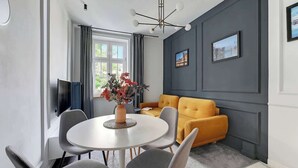 Ein modernes Wohnzimmer mit einem runden Esstisch, grauen Stühlen, einem gelben Sofa und einem Flachbildfernseher.