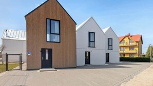 En moderne bygning med træfacade, en hvid bygning med saddeltag, og en gul bygning med rødt tag.