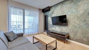 Ein modernes Wohnzimmer mit einer Couch, einem Couchtisch, einem Flachbildfernseher an einer strukturierten Wand und einer Glastür, die zu einem Außenbereich führt.