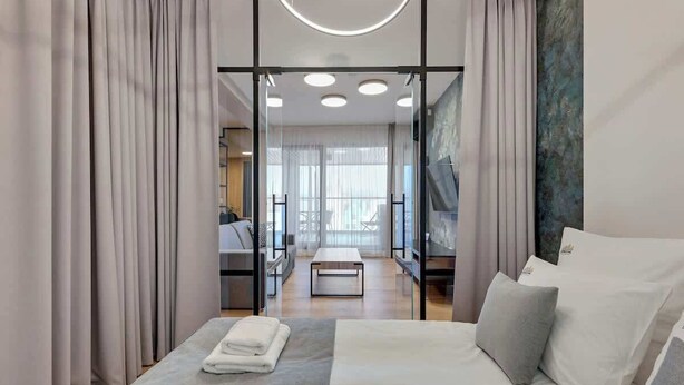 Ein modernes Hotelzimmer mit Bett, einem kleinen Tisch und Blick durch eine Glastür.